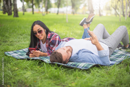 loving couple sitting on a plaid blanket in the park and use the phone, handsome guy and girl © Vasiliy