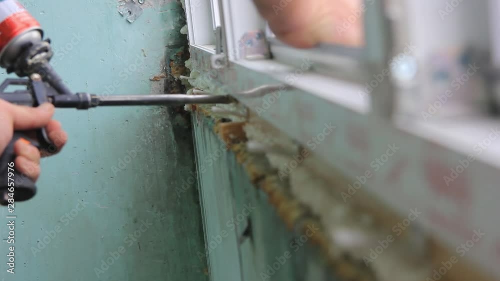 Worker is applying polyurethane foam to fill gap between sash and