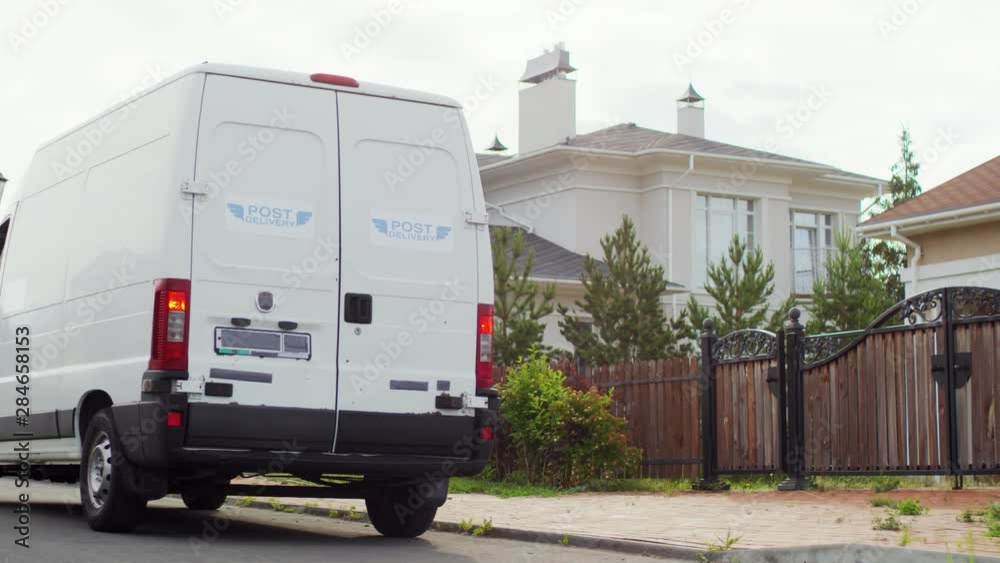 Medium shot of male postal service worker in blue uniform parking mail delivery van and taking out package