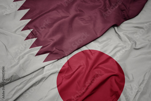 waving colorful flag of japan and national flag of qatar.