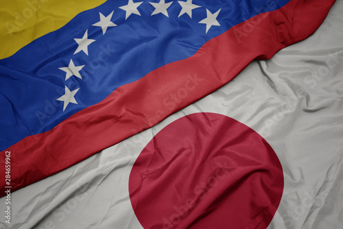 waving colorful flag of japan and national flag of venezuela.