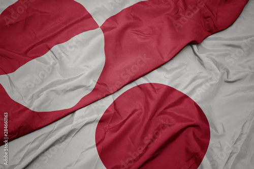 waving colorful flag of japan and national flag of greenland.