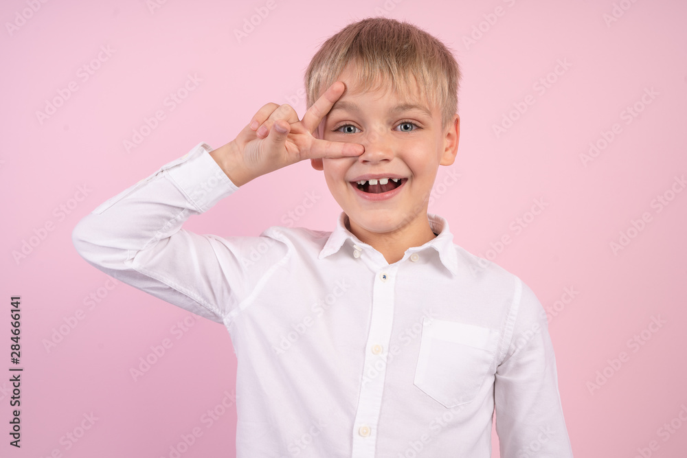 Portrait of naughty little boy smiling and showing peace sign. studio portrait over pink background. wearing white shirt. Portrait of naughty little boy smiling and showing peace sign. studio portrait over pink background. wearing white shirt.
