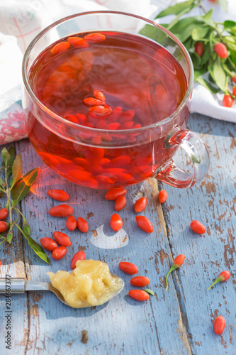 Fresh goji berries tea in a glass cup on a wooden table, healthcare and healthy eating concept