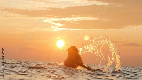 silhouette of a woman tumbling out of the water making a circle with hair with splashes of drops at dawn, a girl swimming in the sea enjoying sunrise, summer vacation concept