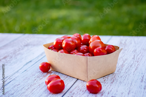 Organic ripe cherry tomatoes in a recyclable paper box on a wooden tablein the garden. Cooking ingredients. Harvest. Sustainable living. Say “no” to plastic packaging. photo