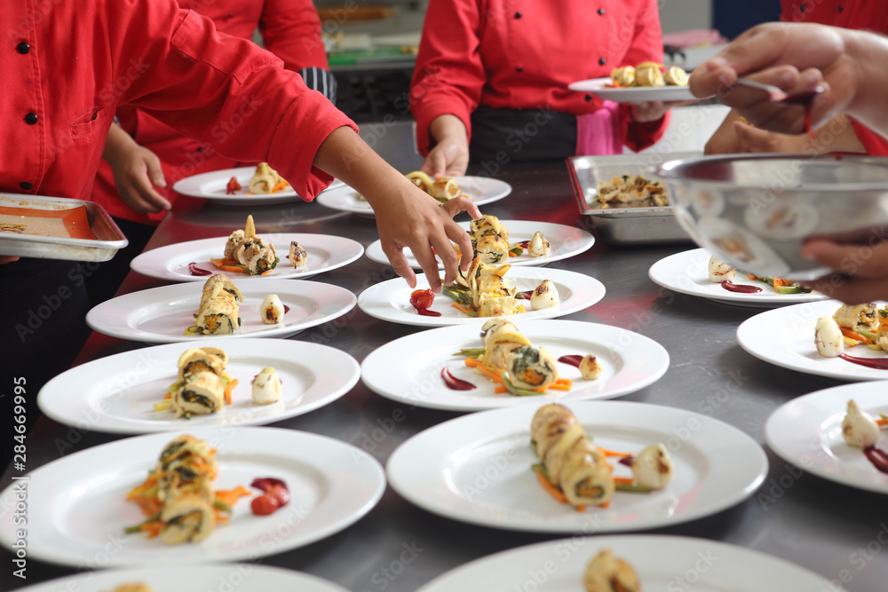 The hands of chefs prepare various dishes for a banquet that includes roasted chicken fillet and dessert. The hands of chefs prepare various dishes for a banquet that includes roasted chicken fillet and dessert.