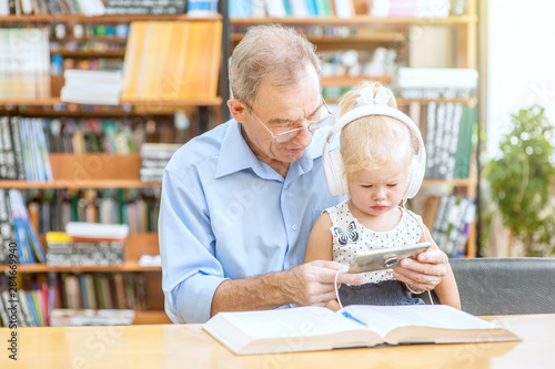 Senior man with a little girl is using a smartphone in the library