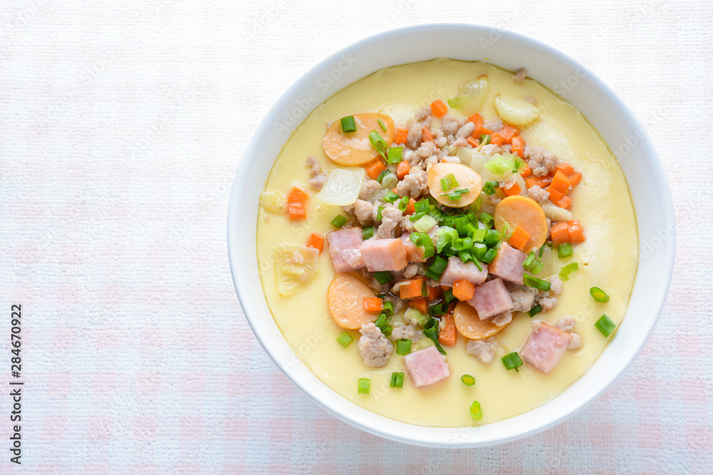 Steamed egg custard cuisine in a white bowl with minced pork, sausage and bacon.  Or Only with egg, water, salt and some sesame oil, you can make this super smooth custard at home.