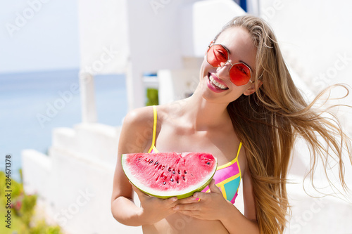 All Inclusive Cheap Summer Holidays. Young Happy Woman with Watermelon and pink sunglasses at beach Background. Summertime fun weekend. Beautiful girl in summer outfit. Selective focus. Hot Vacation