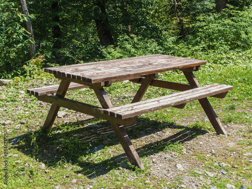 An old table and benches stands on the green grass in forest