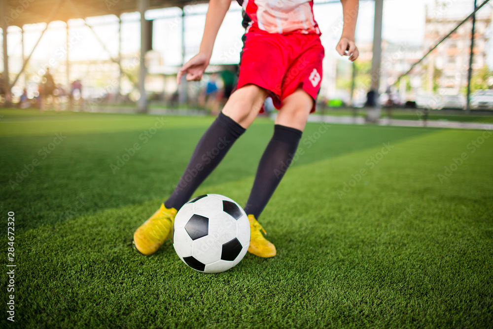 kid soccer player speed run to shoot ball to goal on artificial turf with blurry soccer player background. Soccer player training in football academy.
