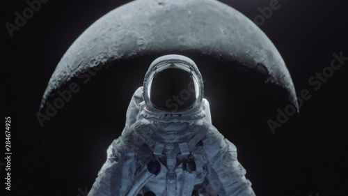 Dolly shot of an astronaut in spacesuit with moon in the background.