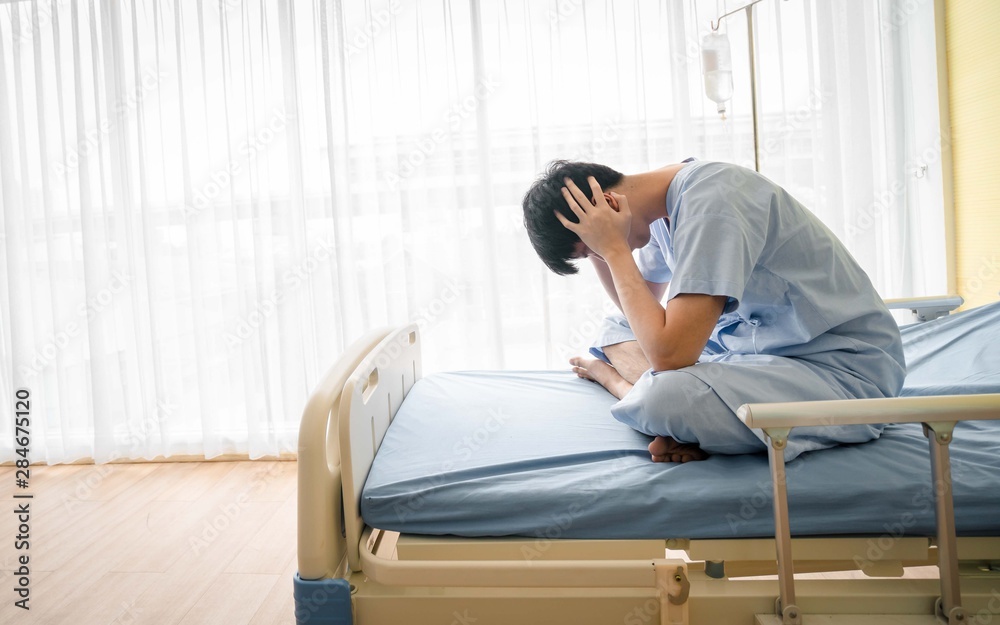 Patient asian man 25 year old Wear a sick suit feeling unwell and worry, sit in a bed at hospital. Asian patient young male 25s is a flu feel not good sit on a bed in the room. white background
