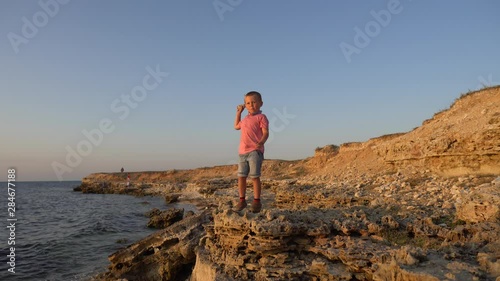 Child boy pick up a stone and throw it in a sea . Real emotions, boy on a sky background. Real positive emotions, real time video footage, boy on a blue sky background, 4K