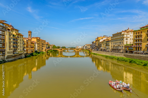 St Trinity Bridge stone bridge and boats on Arno River water and embankment promenade with buildings in historical centre of Florence Tuscany, Italy