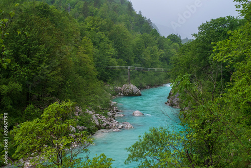 Die Soca im Tal mit einer Br  cke bei regnerischen Wetter und Wolken