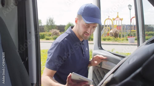 Handheld shot of male postal service worker with tablet getting into delivery van and preparing to drive away