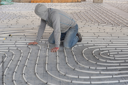 HVAC technician working on underfloor heating system installation. Close up on water floor heating system interior of a new indoor swimming pool and SPA center. Plumbing pipes. Individual Heating.