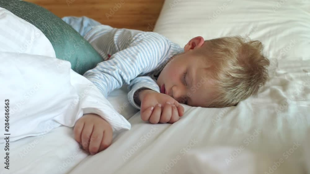 Close-up of a small blond boy sleeping soundly on a white bed. Slow motion. Adorable little boy sleeping in bed. Close-up of a small blond boy sleeping soundly on a white bed. Slow motion. Adorable little boy sleeping in bed.