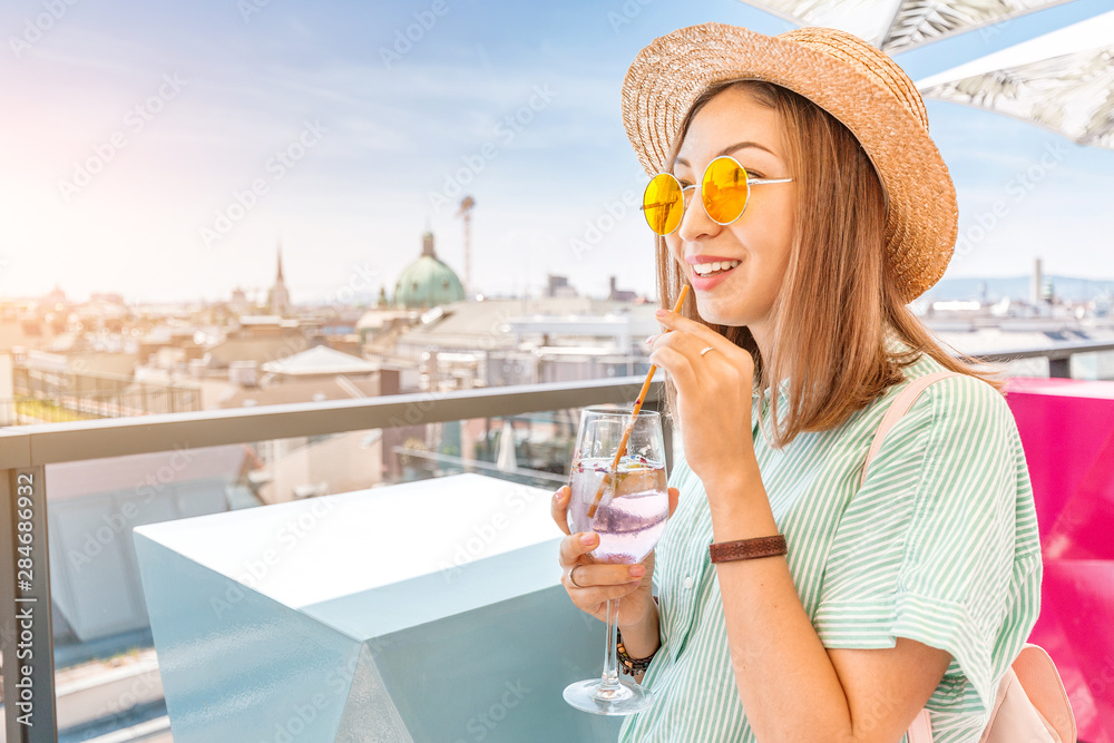 Closeup of asian woman drinking cocktail in open bar terrace on a rooftop with great view of Vienna city