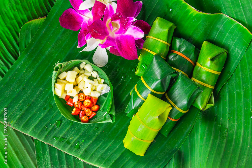 traditional thai food style sour porks wrapped with banana leaf decorated with ingredient orchid flower, top view