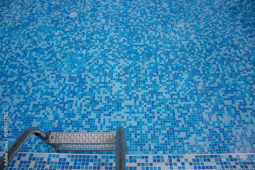 Close up of a blue hotel Swimming pool with blue mosaic tiles of the pool and ladder going down to the water.