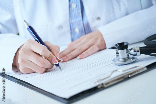 Female medicine doctor hand holding silver pen writing something on clipboard closeup.. Ward round, patient visit check, medical calculation and statistics concept.