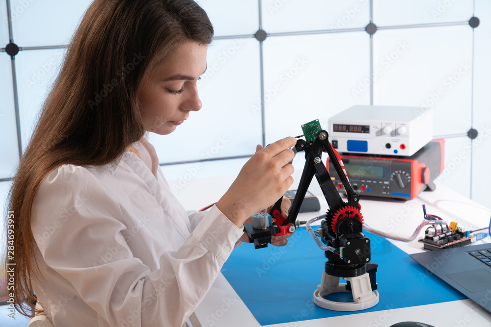 A young woman writes an algorithm for the robot arm. Science Research Laboratory for Robotic Arm Model. Computer Laboratory A young woman writes an algorithm for the robot arm. Science Research Laboratory for Robotic Arm Model. Computer Laboratory