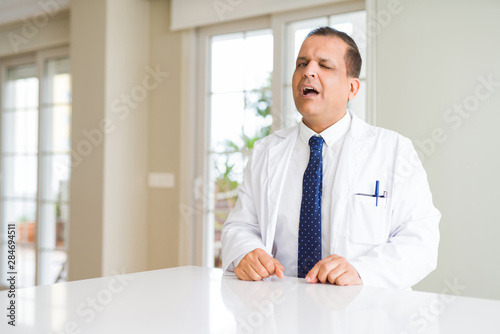 Middle age doctor man wearing medical coat at the clinic winking looking at the camera with sexy expression, cheerful and happy face.