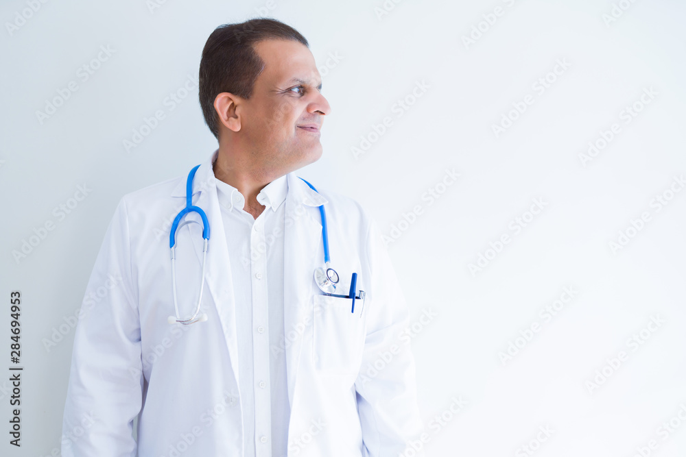 Middle age doctor man wearing stethoscope and medical coat over white background looking to side, relax profile pose with natural face with confident smile. Middle age doctor man wearing stethoscope and medical coat over white background looking to side, relax profile pose with natural face with confident smile.