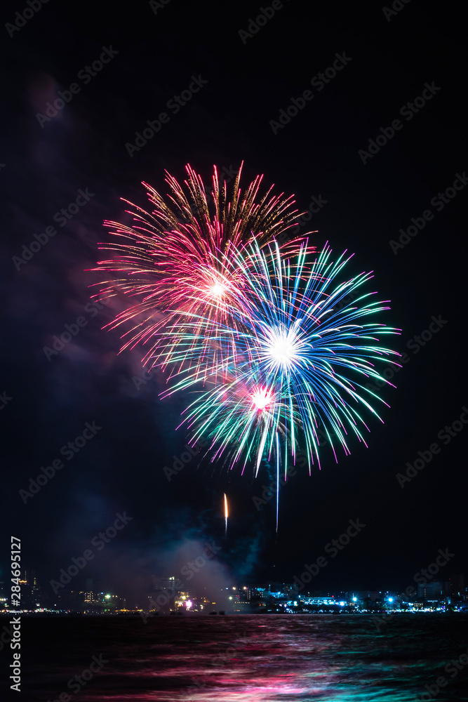 Fireworks over sea with city night on background. Festive colorful fireworks celebration in night sky. Fireworks over sea with city night on background. Festive colorful fireworks celebration in night sky.