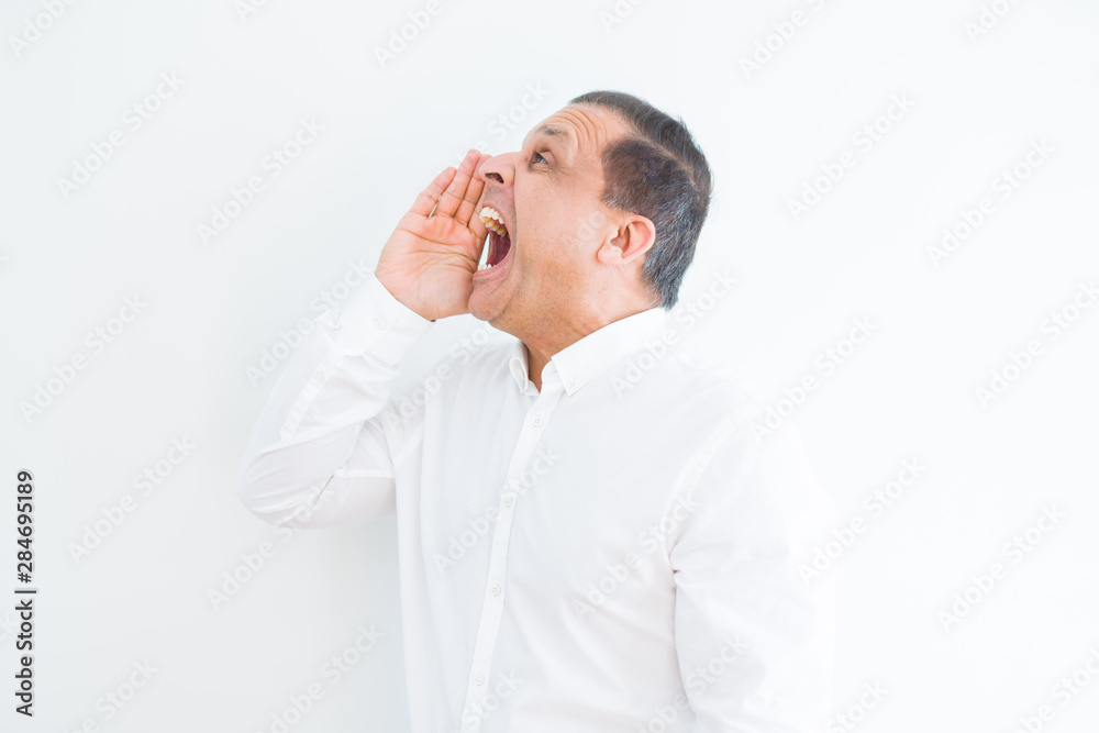 Middle age man shouting crazy with hands over mouth over white wall background Middle age man shouting crazy with hands over mouth over white wall background