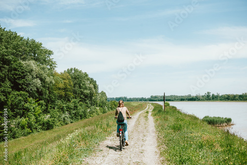 Rear view of young cyclist woman riding a bike near the large Rhine river which separates France from Germany