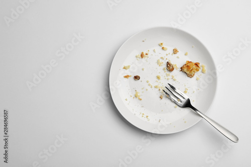 Dirty plate with food leftovers and fork on white background, top view
