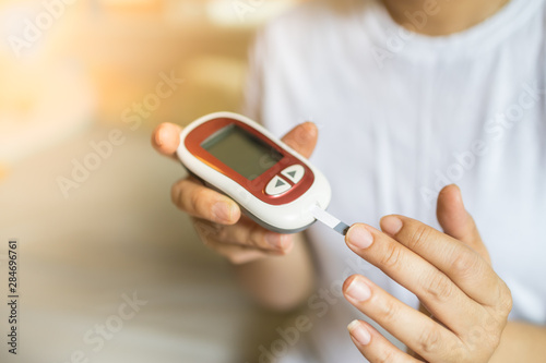 Close up of woman hands using Glucose meter on finger to check blood sugar level. Use as Medicine, diabetes, glycemia, health care and people concept. photo