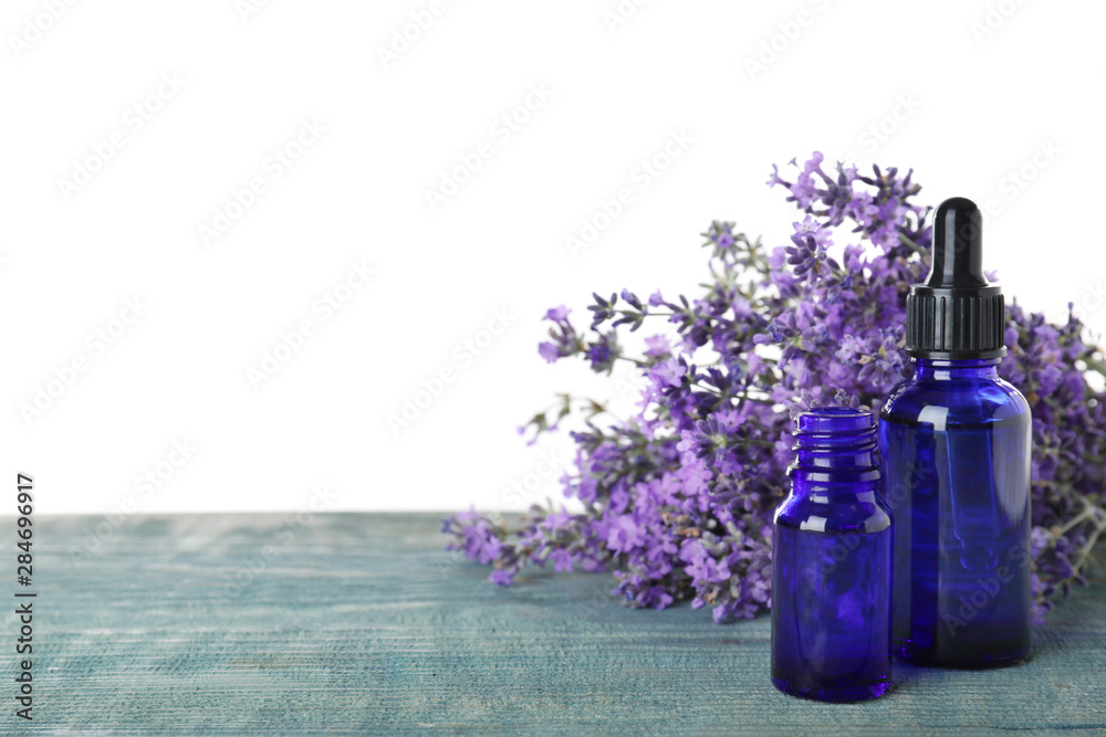 Bottles of essential oil and lavender flowers on blue wooden table against white background Bottles of essential oil and lavender flowers on blue wooden table against white background