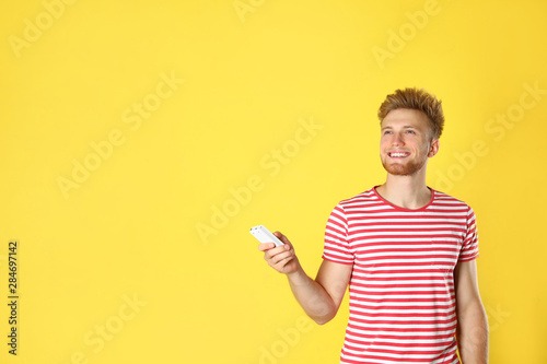 Young man with air conditioner remote on yellow background. Space for text