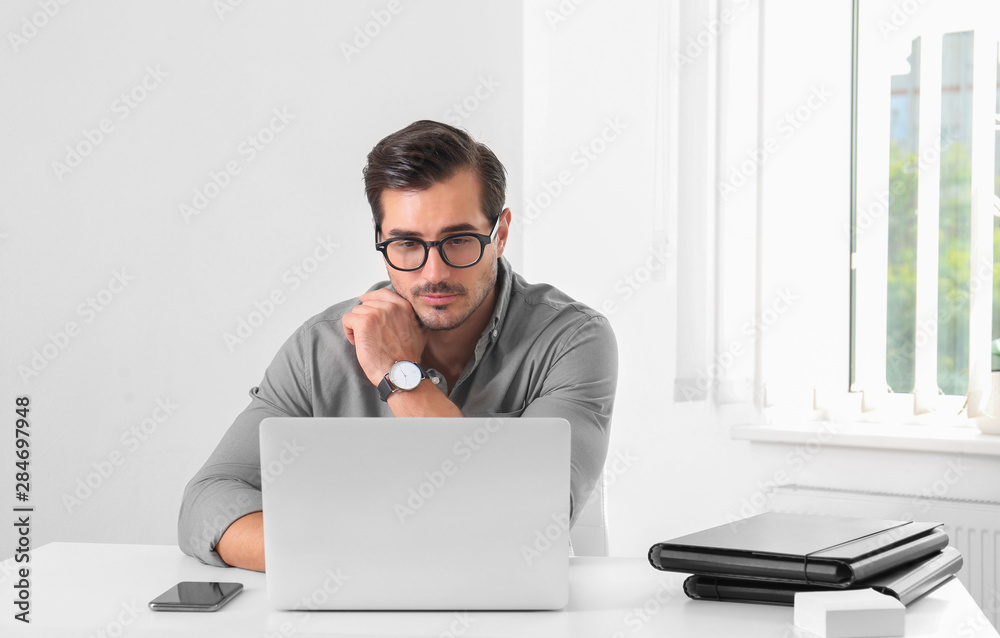 Handsome young man working with laptop at table in office Handsome young man working with laptop at table in office