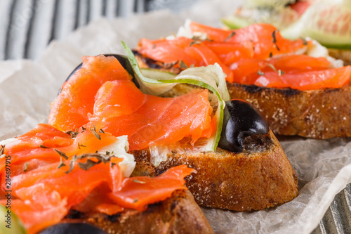 Bruschetta with smoked salmon, fresh cucumber, black olives and camembert on crumpled baking paper