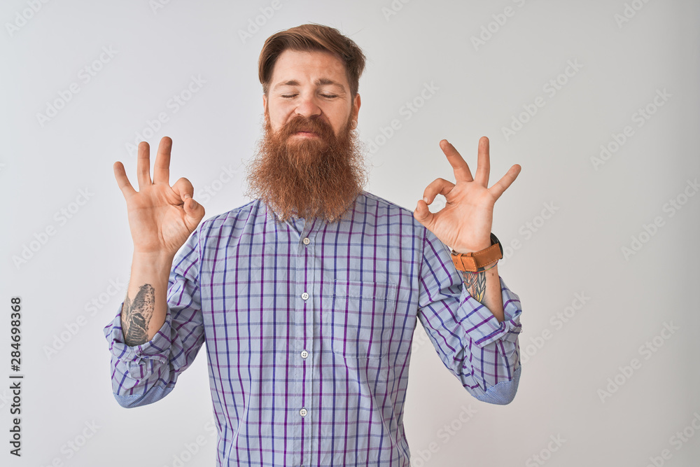 Young redhead irish man wearing casual shirt standing over isolated white background relax and smiling with eyes closed doing meditation gesture with fingers. Yoga concept. Young redhead irish man wearing casual shirt standing over isolated white background relax and smiling with eyes closed doing meditation gesture with fingers. Yoga concept.