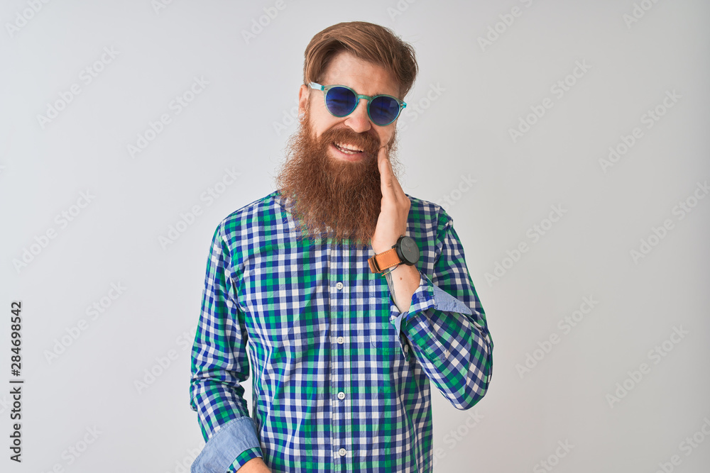 Young redhead irish man wearing casual shirt and sunglasses over isolated white background touching mouth with hand with painful expression because of toothache or dental illness on teeth. Young redhead irish man wearing casual shirt and sunglasses over isolated white background touching mouth with hand with painful expression because of toothache or dental illness on teeth.