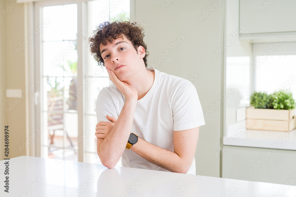 Young handsome man wearing white t-shirt at home thinking looking tired and bored with depression problems with crossed arms. Young handsome man wearing white t-shirt at home thinking looking tired and bored with depression problems with crossed arms.