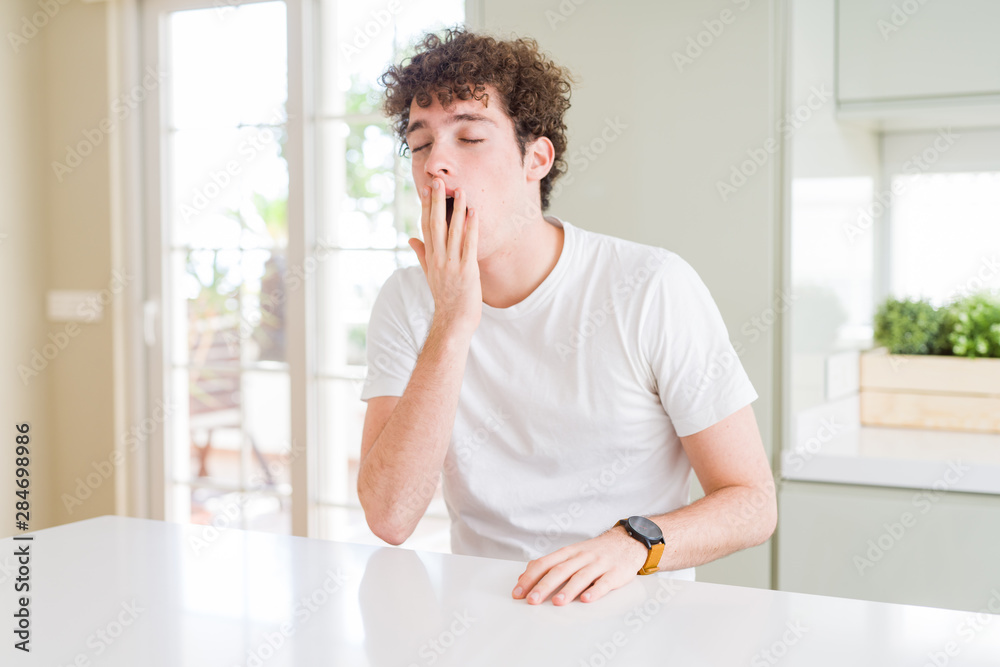 Young handsome man wearing white t-shirt at home bored yawning tired covering mouth with hand. Restless and sleepiness. Young handsome man wearing white t-shirt at home bored yawning tired covering mouth with hand. Restless and sleepiness.