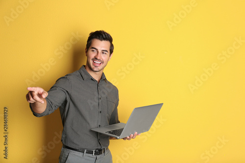 Young male teacher with laptop on yellow background. Space for text