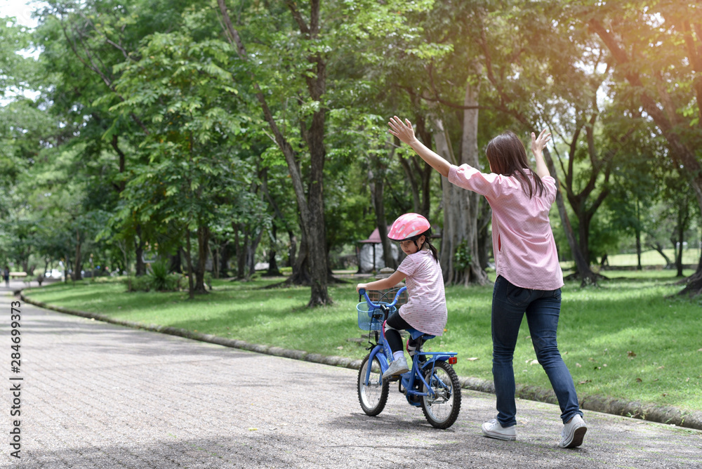 Fototapeta premium Mother teaching her daughter riding bicycle.Little girl wearing safety equipment.