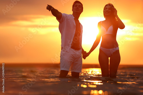 Happy young couple spending time together on sea beach at sunset