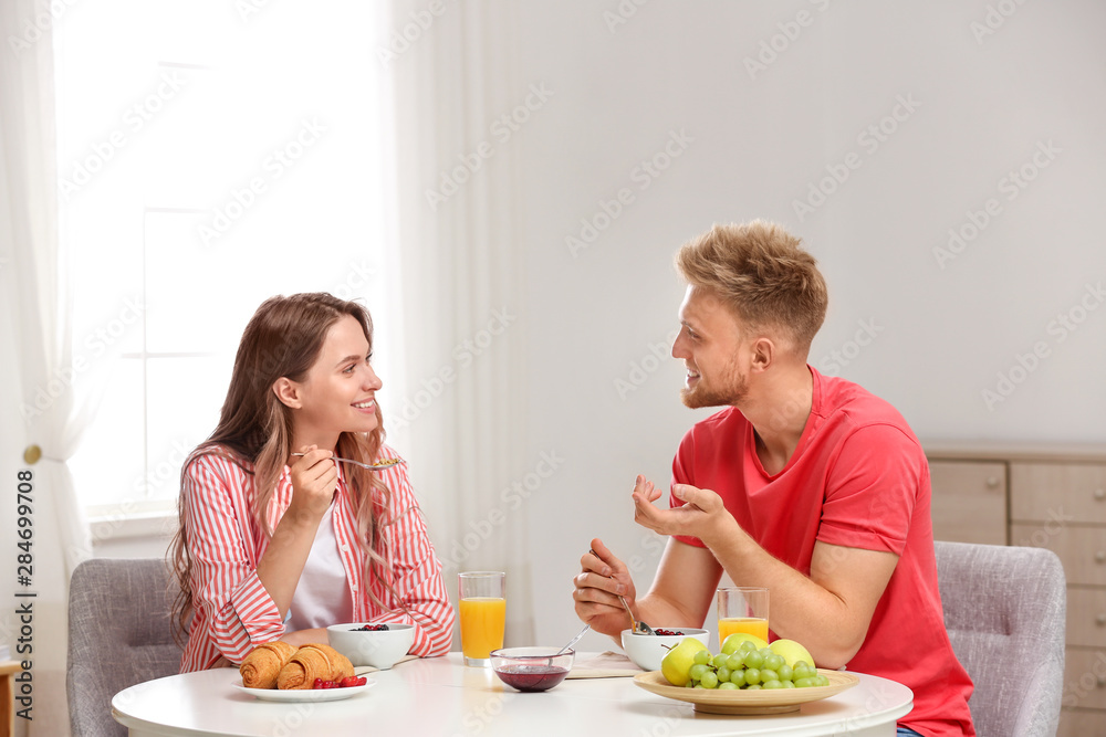 Happy young couple having breakfast at table in room