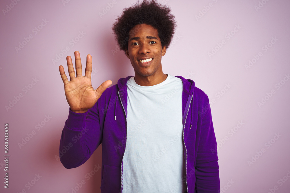 Young african american man wearing purple sweatshirt standing over isolated pink background showing and pointing up with fingers number five while smiling confident and happy. Young african american man wearing purple sweatshirt standing over isolated pink background showing and pointing up with fingers number five while smiling confident and happy.