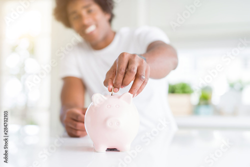 Close up of african american man saving money putting a coin inside piggy bank photo